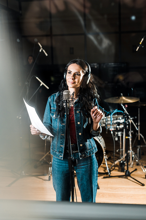 selective focus of inspired woman in headphones standing near microphone in recording studio