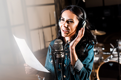 selective focus of beautiful smiling woman in headphones singing in recording studio