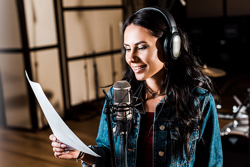 pretty woman in headphones singing in recording studio near microphone
