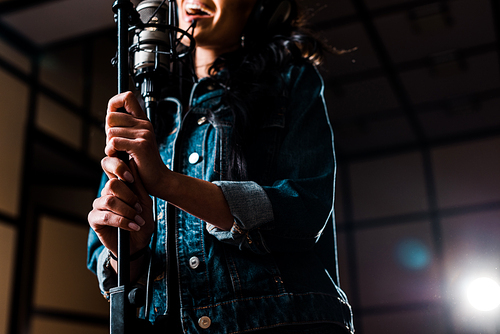 partial view of woman singing near microphone in recording studio