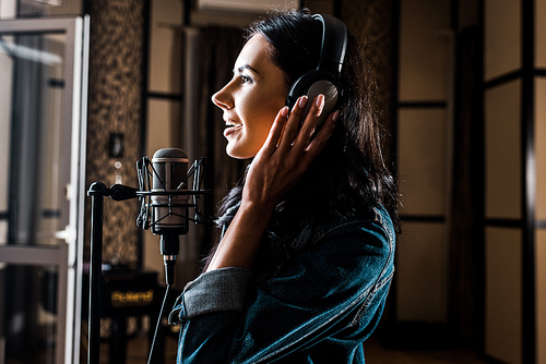 side view of beautiful woman singing near microphone in recording studio