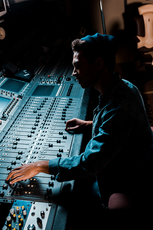 sound producer working at mixing console in dark recording studio