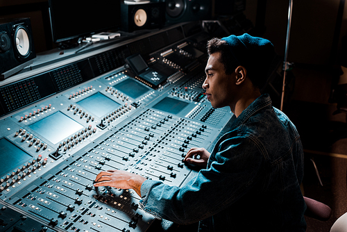 concentrated mixed race sound producer working at mixing console in dark recording studio