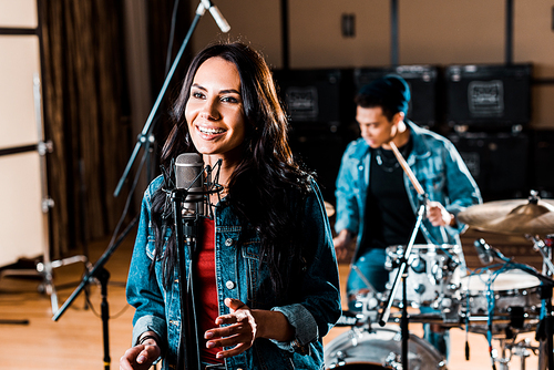pretty woman singing while mixed race musician playing drums in recording studio
