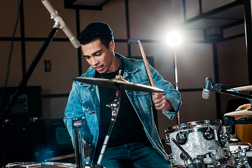 handsome, inspired mixed race musician playing drums in recording studio