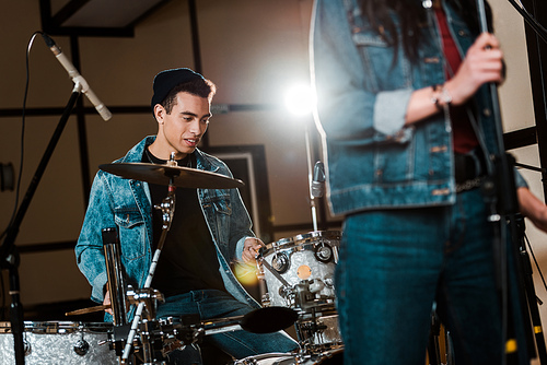 selective focus of handsome mixed race musician playing drums while woman singing in recording studio