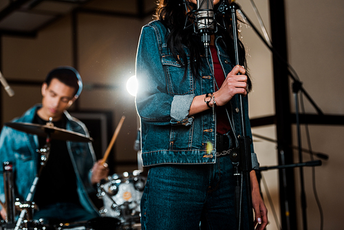 selective focus of woman singing in recording studio while mixed race musician playing drums