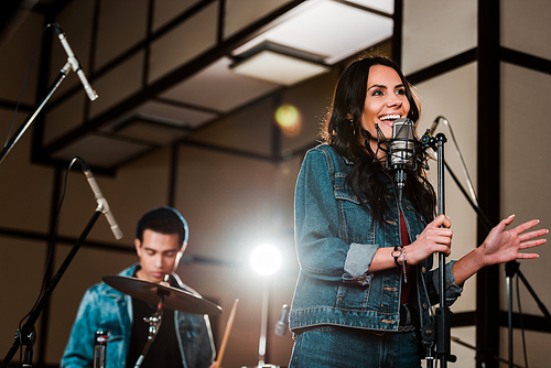 selective focus of excited woman singing in recording studio while handsome mixed race musician playing drums