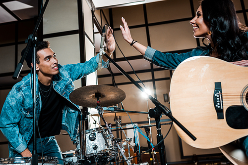 young smiling multicultural musicians giving high five in recording studio