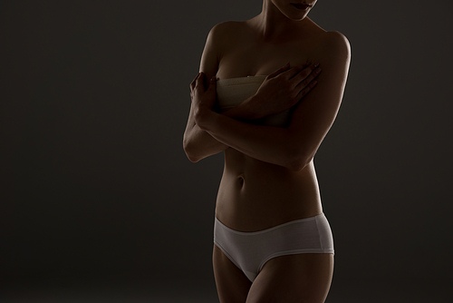 cropped view of woman in panties with breast bandage in darkness