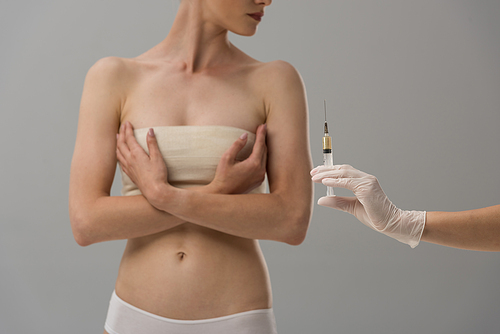 cropped view of patient with breast bandage and doctor in latex glove holding syringe isolated on grey