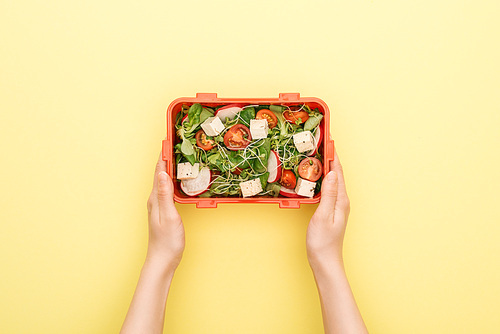 cropped view of woman holding lunch box with salad in hands on yellow background
