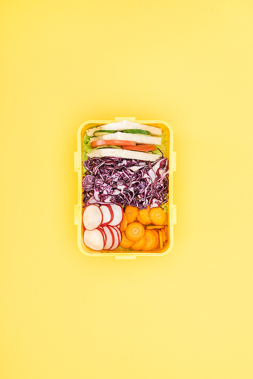 top view of lunch box with sandwiches and vegetables on yellow background