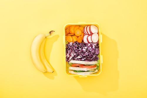 top view of lunch box with sandwiches and vegetables near bananas