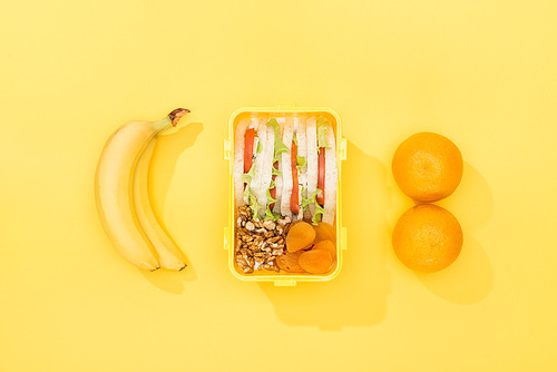 top view of nuts, dried apricots with sandwiches in lunch box near bananas and oranges