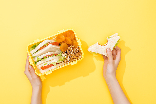 cropped view of lunch box with nuts, dried apricots and sandwiches in woman hands