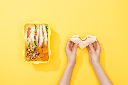 cropped view of woman hold sandwich near lunch box with nuts, dried apricots and snacks