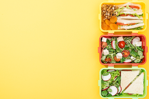 top view of three lunch boxes with food  on yellow background