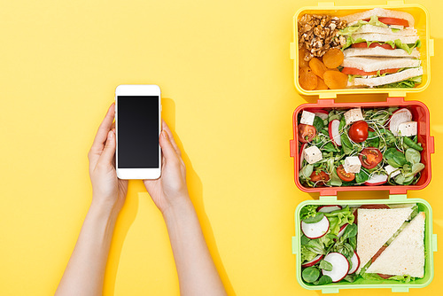 cropped view of woman holding smartphone near lunch boxes with food