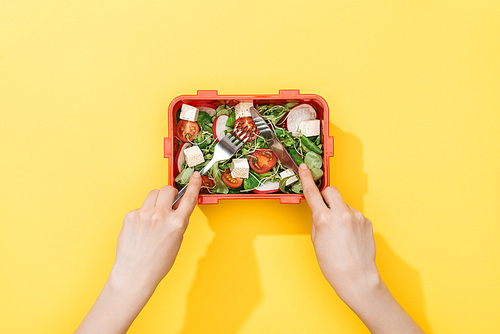 cropped view of woman holding fork and knife, eating salad from lunch box