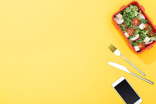 top view of lunch box with salad near fork, knife and smartphone