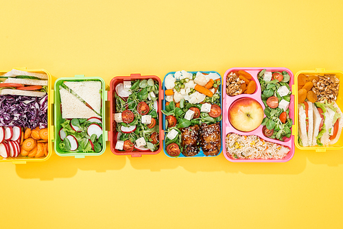 top view of lunch boxes with delicious food on yellow background