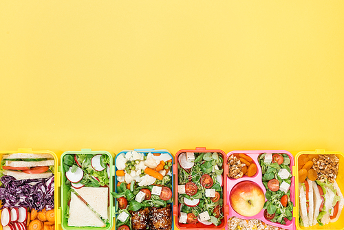 top view of lunch boxes with food on yellow background with copy space