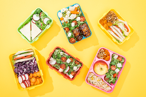top view of lunch boxes with fresh food on yellow background