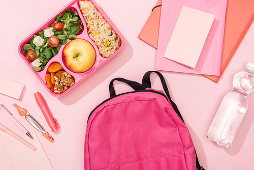 top view of backpack, lunch box with food and stationery on pink background