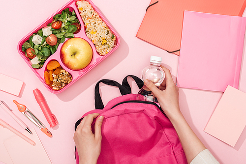 cropped view of woman packing backpack near lunch box and stationery