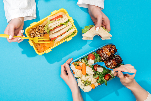 cropped view of two women holding forks over lunch boxes with food