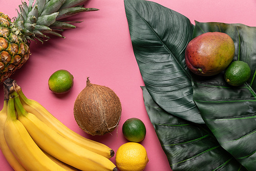 whole ripe tropical fruits with green leaves on pink background