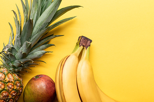 top view of whole ripe bananas, pineapple and mango on yellow background