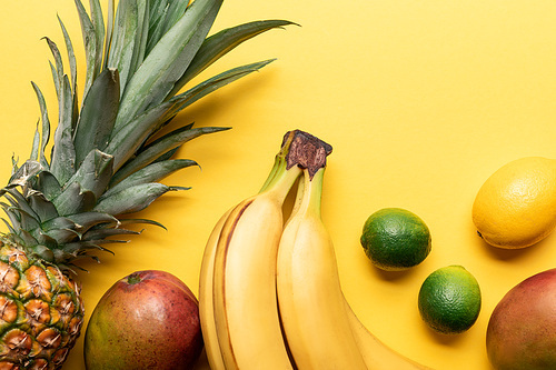 top view of whole ripe bananas, pineapple, citrus fruits and mango on yellow background with copy space