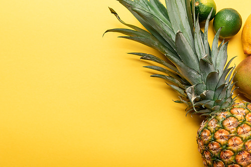 top view of whole ripe pineapple, citrus fruits and mango on yellow background