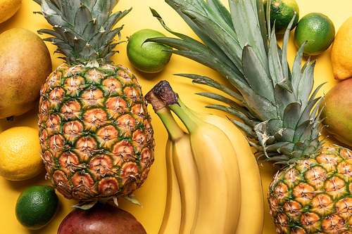 top view of whole ripe bananas, pineapple, citrus fruits and mango on yellow background