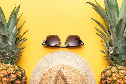 top view of straw hat and sunglasses near pineapples on yellow background