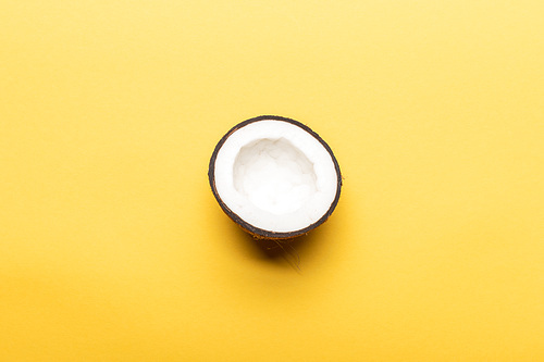 top view of ripe coconut half on yellow background with copy space
