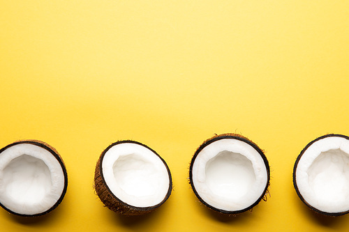 top view of ripe coconut halves on yellow background with copy space