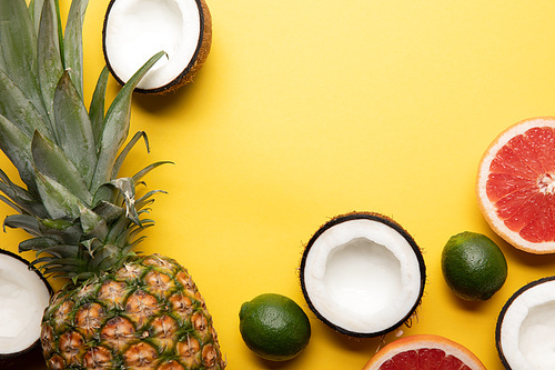 top view of whole ripe pineapple, citrus fruits and coconut halves on yellow background
