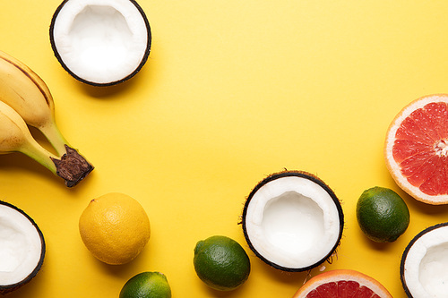 top view of citrus fruits, bananas and coconuts on yellow background with copy space