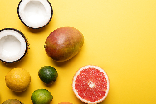 top view of citrus fruits, mango and coconuts on yellow background with copy space