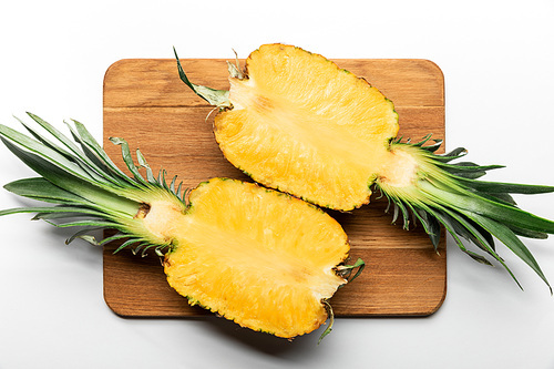top view of cut ripe yellow pineapple on wooden chopping board on white background