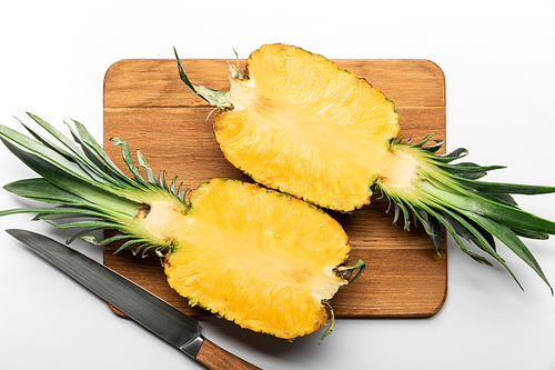 top view of cut ripe yellow pineapple on wooden chopping board with knife on white background
