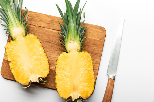 top view of cut ripe pineapple on wooden chopping board with knife on white background