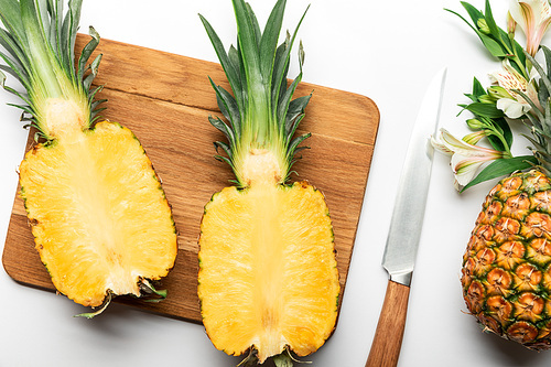 top view of cut ripe yellow pineapple on wooden chopping board near knife and Alstroemeria flowers on white background