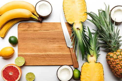 top view of cut and whole tropical fruits on wooden chopping board with copy space near knife on white background