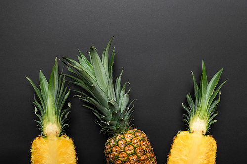 top view of ripe cut and whole yellow pineapples on black background