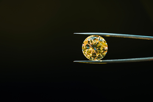 colorful yellow sparkling diamond in tweezers isolated on black
