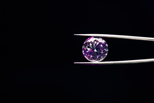 colorful purple sparkling diamond in tweezers isolated on black